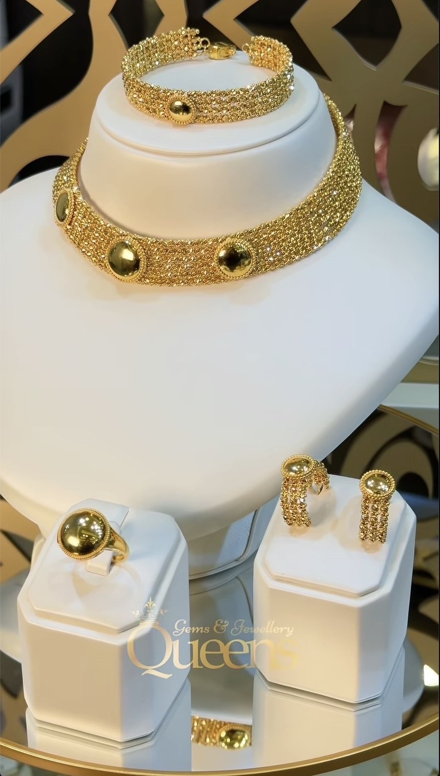 Gold choker, bracelet, ring and earrings displayed on ivory stands