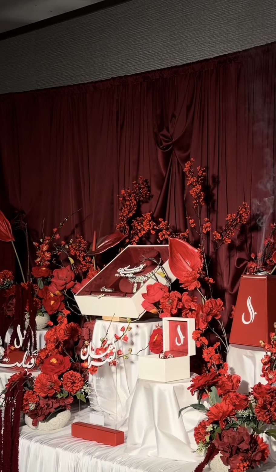 Bridal gift display dressed in deep red flowers, drapes and monogrammed boxes