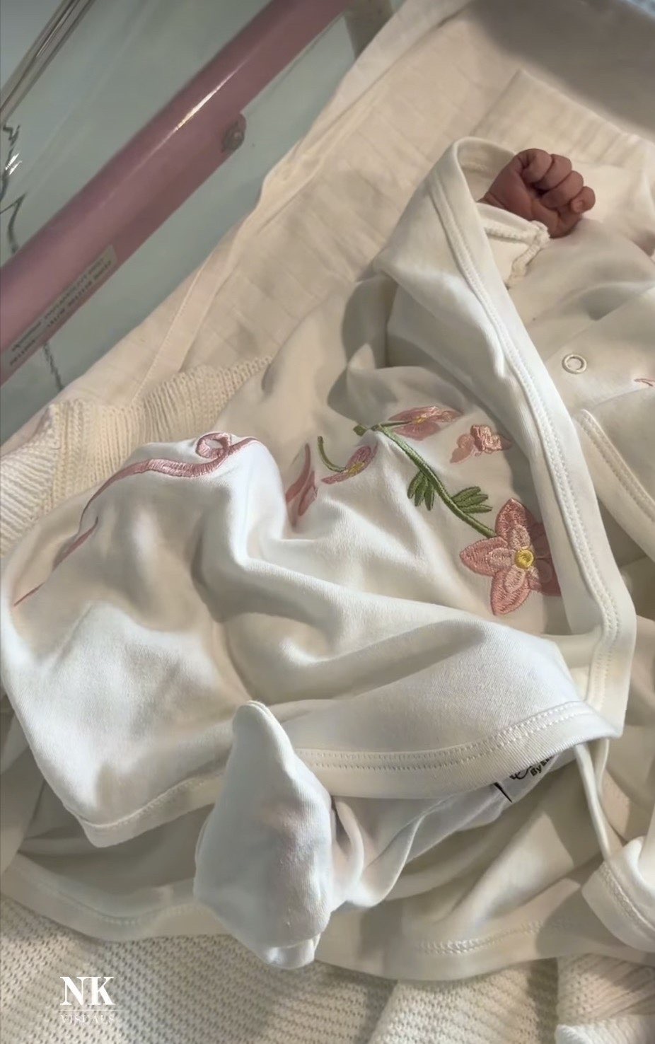 Newborn’s tiny fist peeking from an embroidered white floral outfit